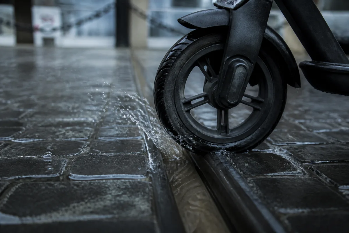 Roue avant de trottinette électrique franchissant un rail de tramway sur une chaussée humide